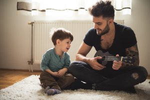 Dad playing some music on a guitar to his son.